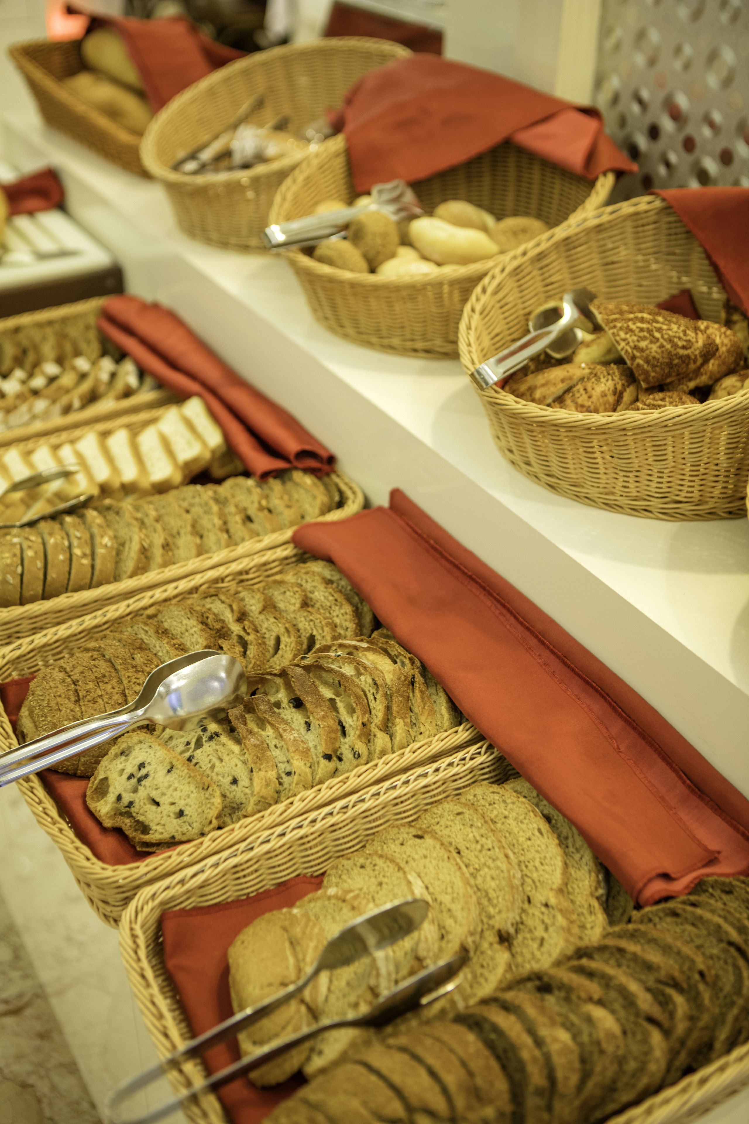 A buffet with various breads and pastries in wicker baskets, each with a spoon.