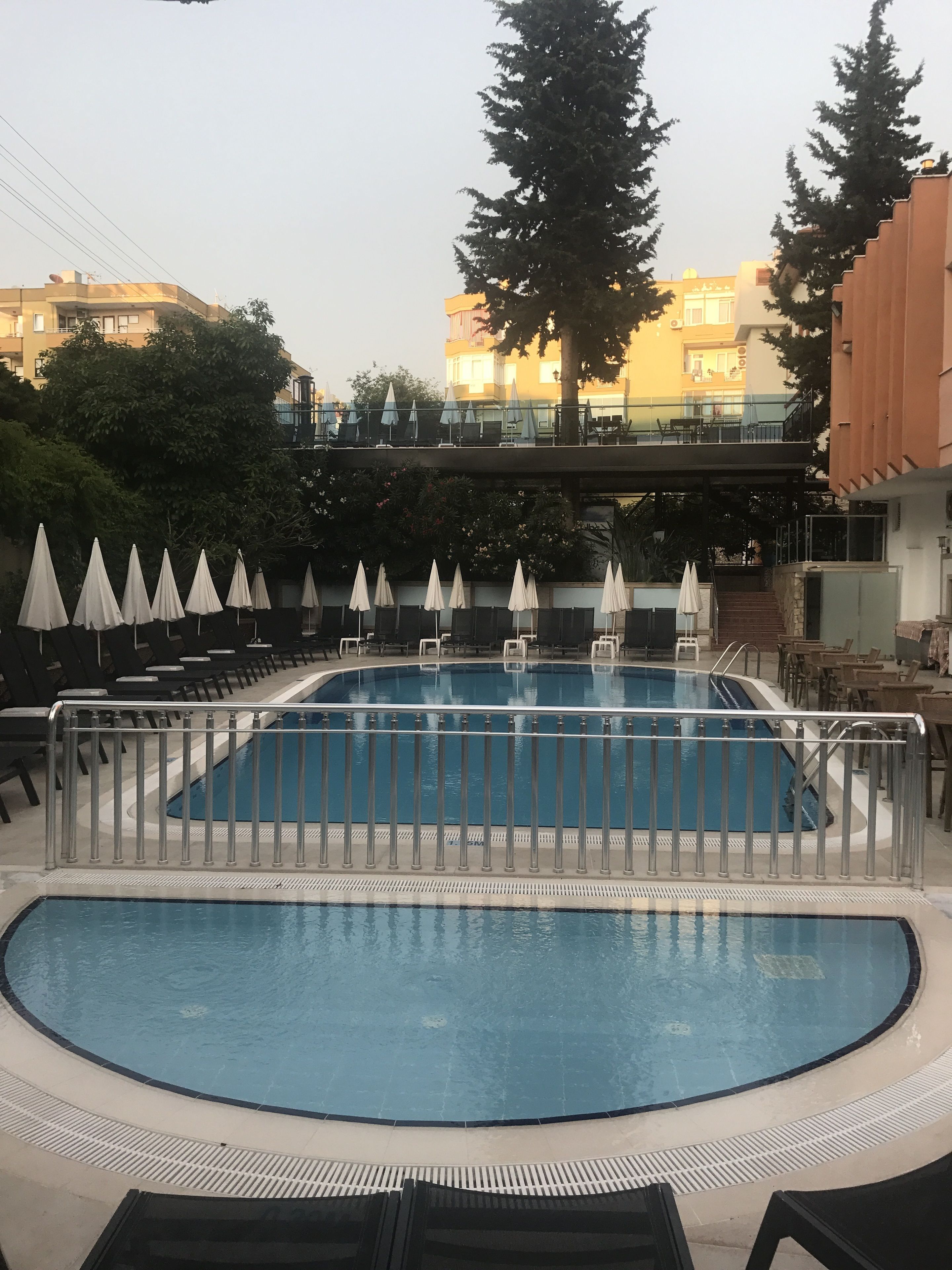 A swimming pool with a surrounding deck, lounge chairs, and umbrellas.