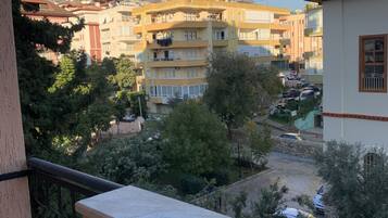 Edificio residencial con varios balcones, un patio de coches y montañas al fondo.