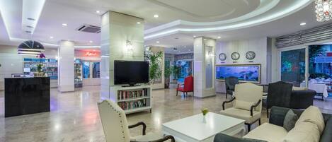 A spacious lobby with a reception desk, a television, a bookshelf, and comfortable seating areas.