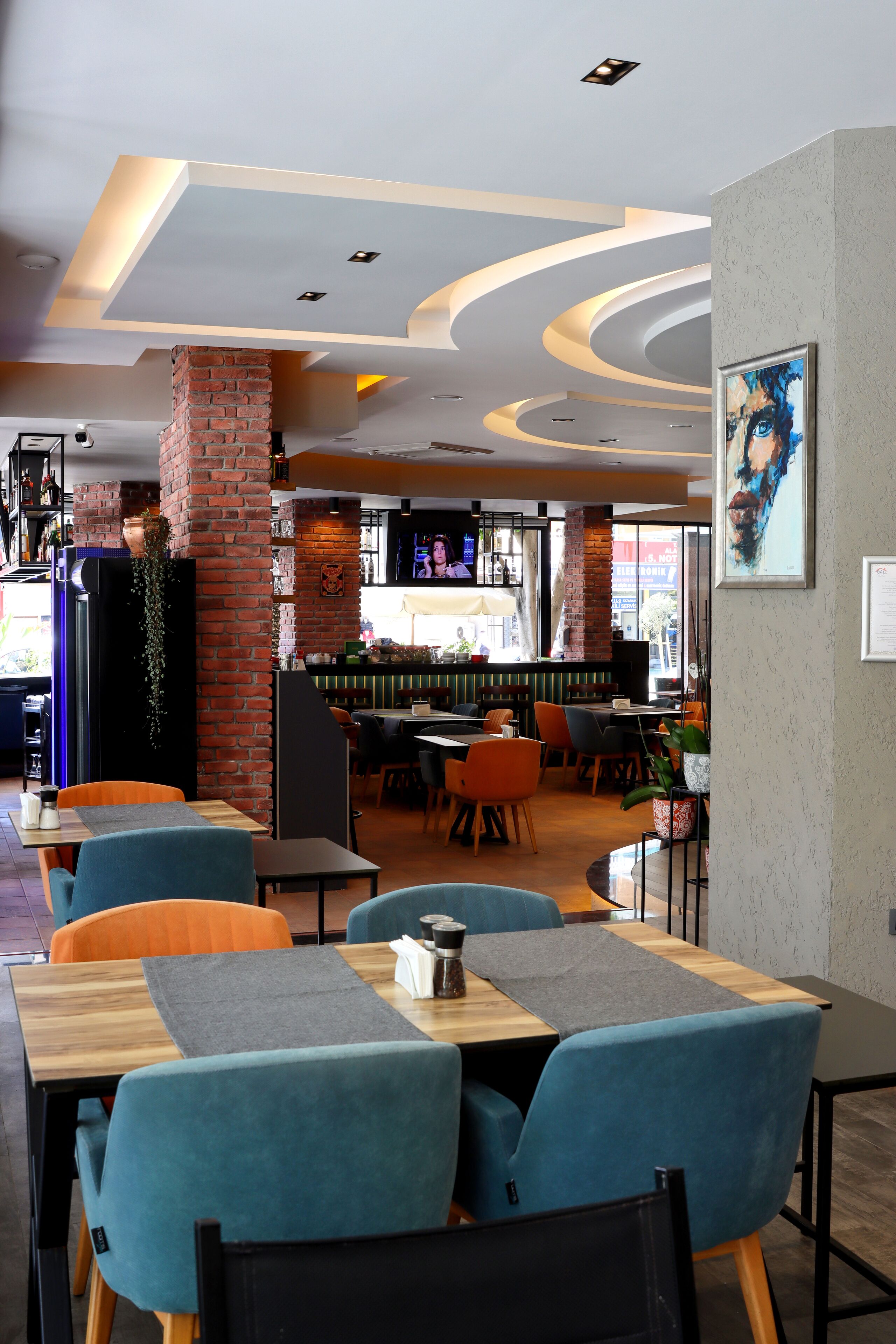 A restaurant interior with wooden tables, blue upholstered chairs, brick pillars, and a modern ceiling design.
