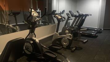 Une salle de sport équipée de plusieurs tapis de course et de vélos d’appartement, d’un grand miroir et d’un sol carrelé.