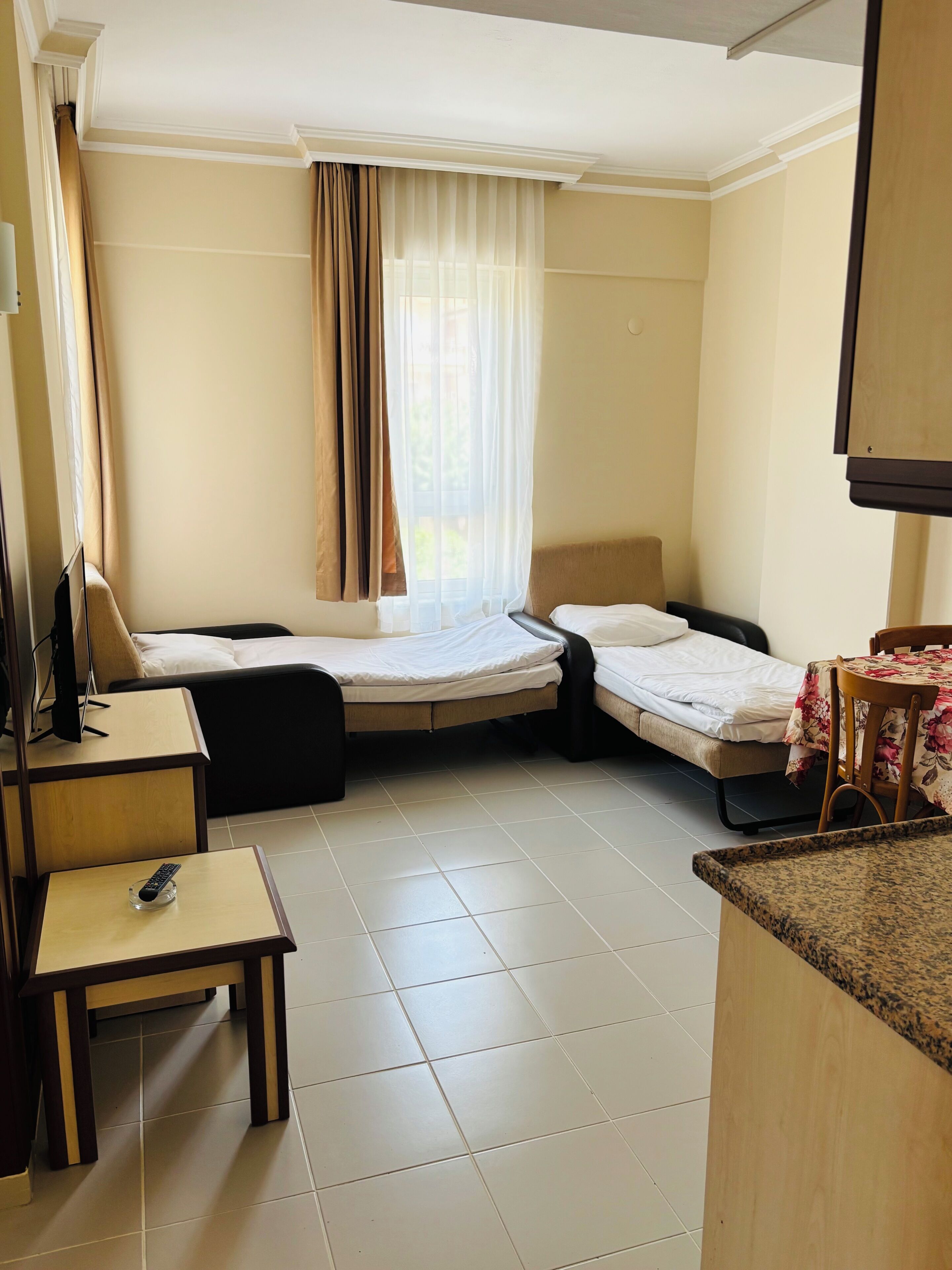A hotel room with two beds, a desk, a chair, a TV, and a window with curtains.