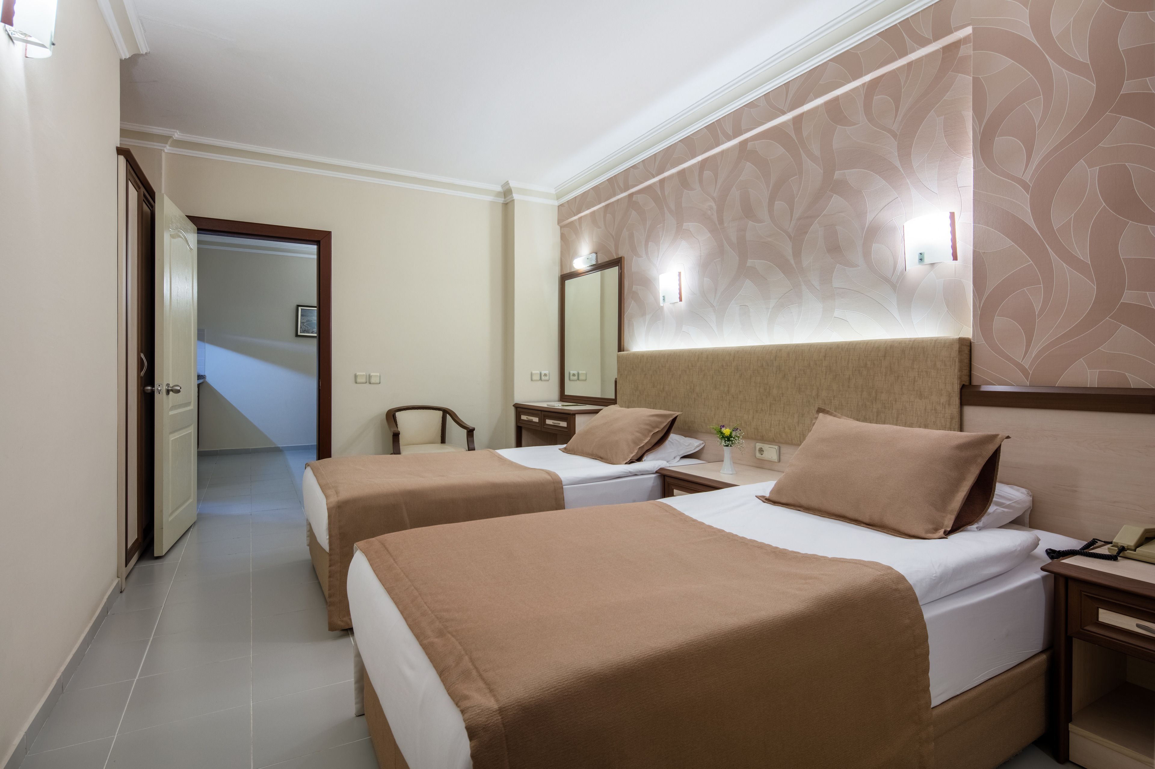 A hotel room with two single beds, a nightstand, a bedside table, a mirror, and a door leading to a hallway.