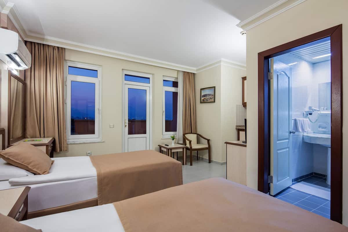Habitación de hotel con dos camas, un escritorio, una silla y un baño visible a través de una puerta abierta.