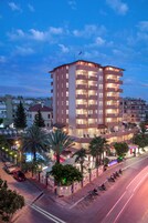 Un hotel de varios pisos con balcones, piscina y un estacionamiento con motocicletas.