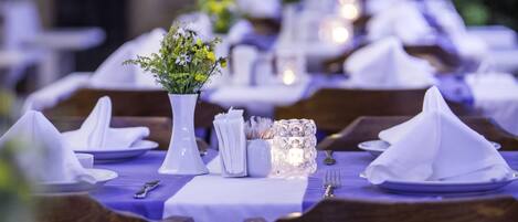 Un comedor con mesas dispuestas para el servicio, con manteles blancos, servilletas y un jarrón con flores.