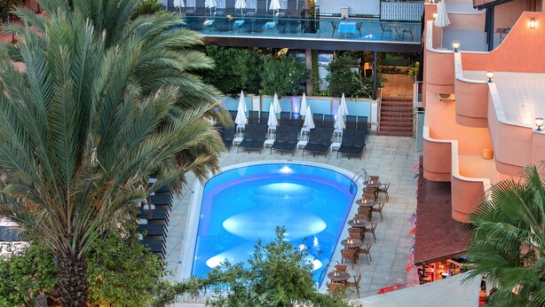 A rooftop pool with lounge chairs and umbrellas, surrounded by palm trees and a stone wall. - May Flower Apart Hotel (Alanya)