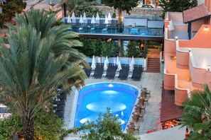 A rooftop pool with lounge chairs and umbrellas, surrounded by palm trees and a stone wall. - May Flower Apart Hotel (Alanya)