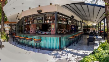 Zona de bar con una barra curva, varios taburetes y una variedad de botellas.