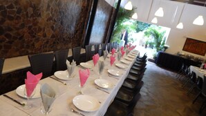 Una larga mesa de comedor dispuesta con platos, vasos y servilletas rosas, con sillas a ambos lados.