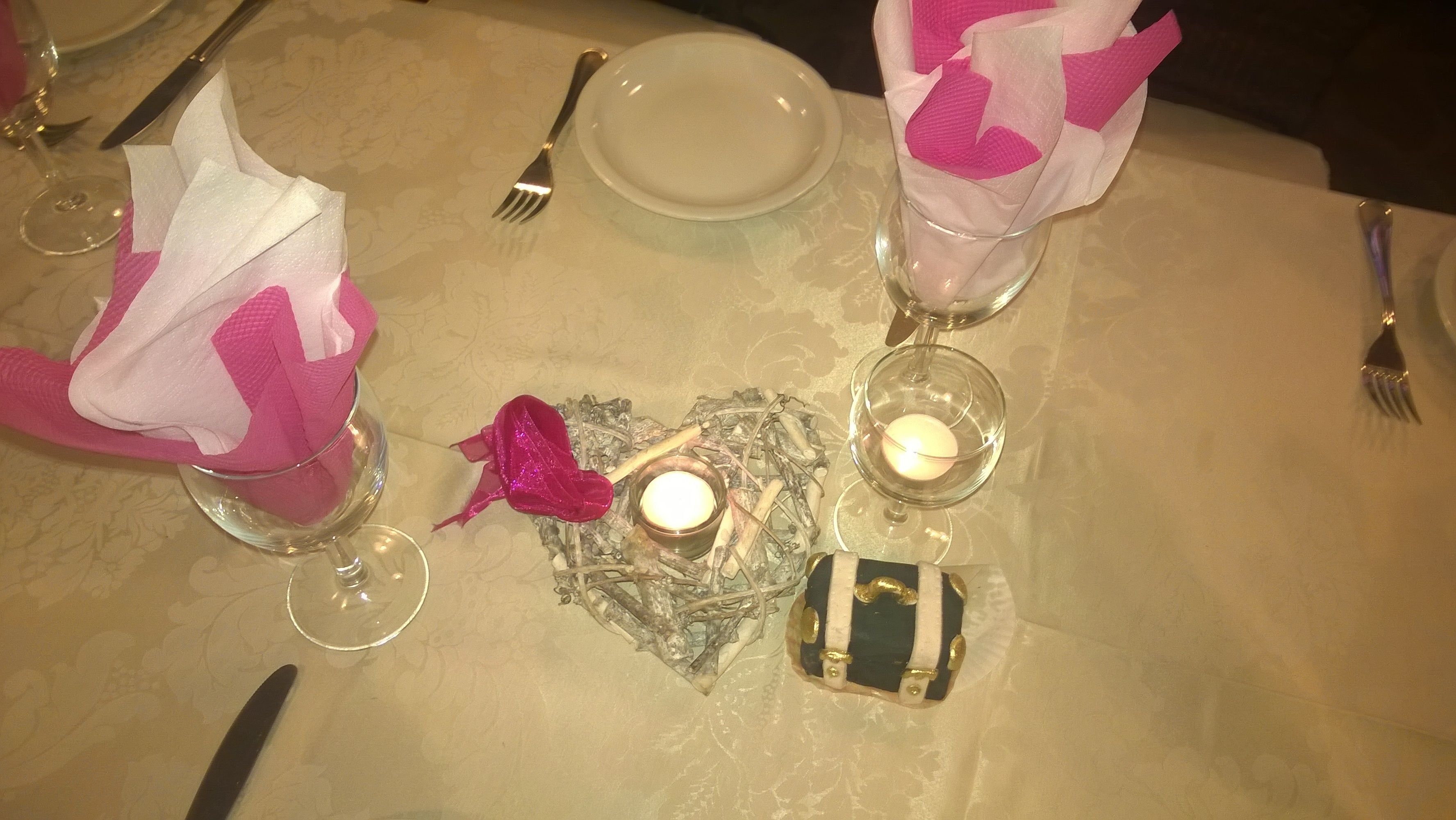 Una mesa dispuesta con un plato blanco, dos vasos y servilletas rosas, una vela y un adorno.