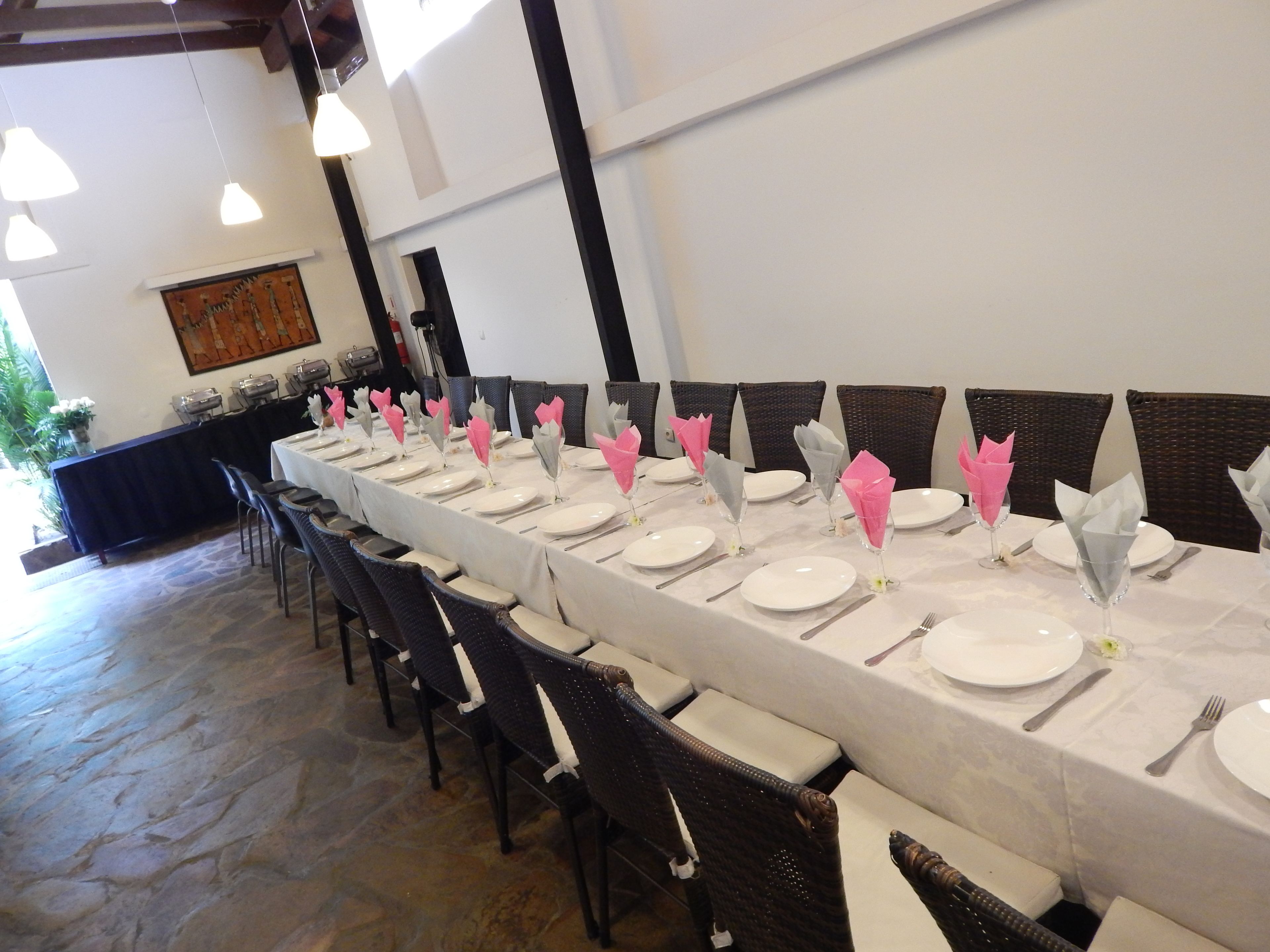 Una larga mesa de comedor dispuesta con platos blancos, cubiertos y servilletas rosas y grises.