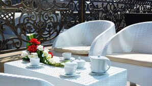 A white wicker table set with tea cups, a teapot, and a floral arrangement. - Admiral Hotel Baku (Baku)