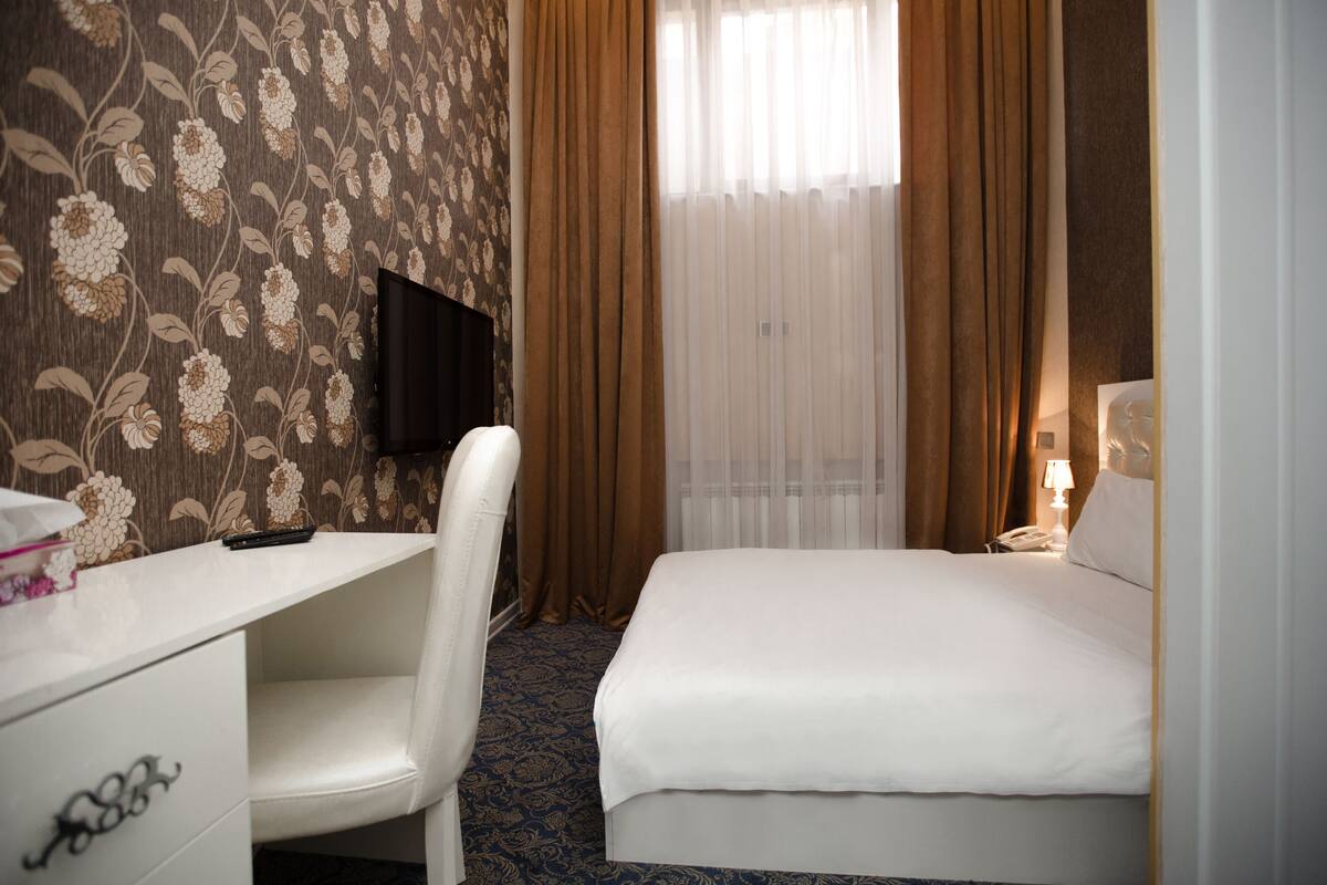 Una habitación de hotel con cama, escritorio, silla, televisor y ventana con cortinas.