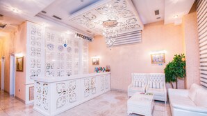 A reception area with a white reception desk, a chandelier, a reception sign, and a seating area with white sofas. - Admiral Hotel Baku (Baku)