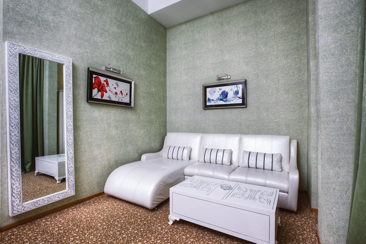 Una habitación con un sofá blanco, una mesita auxiliar blanca, un espejo grande y dos cuadros enmarcados en la pared.