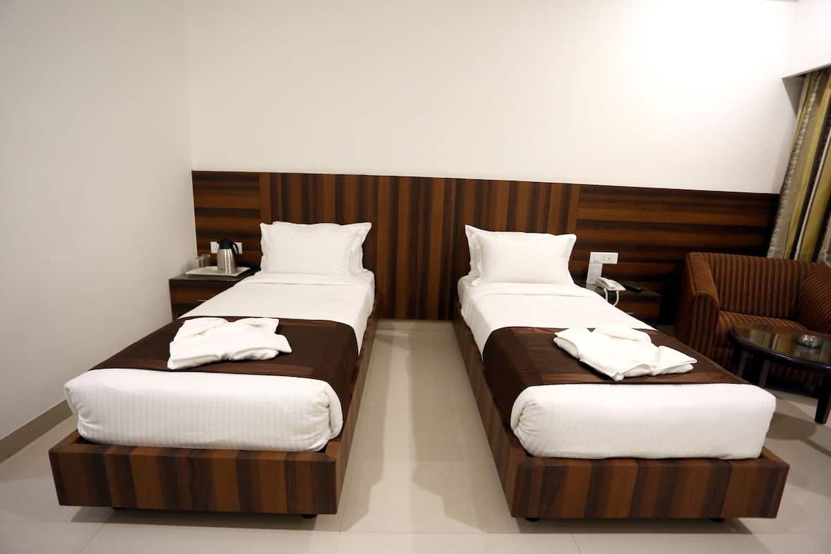 A hotel room with two single beds, a wooden headboard, a small table with a phone, and a chair.