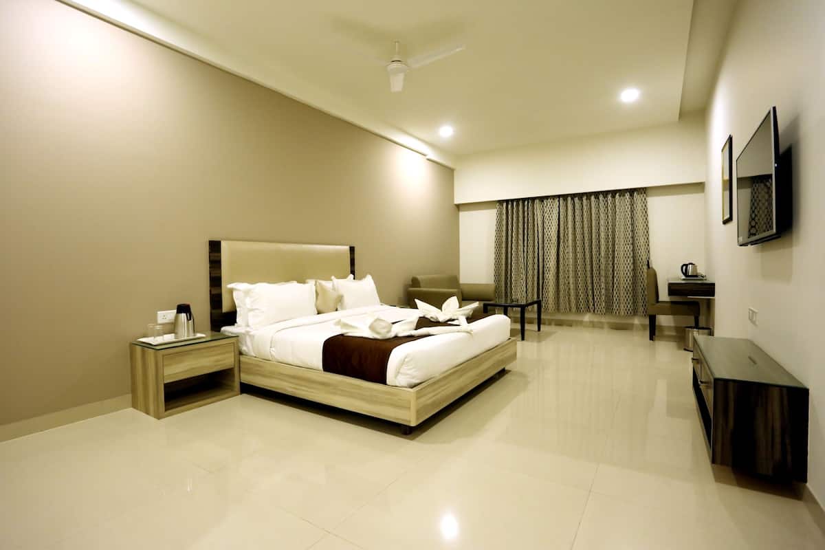 A modern hotel room with a large bed, bedside tables, a desk, a chair, and a flat-screen TV mounted on the wall.