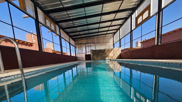 Une piscine intérieure à eau claire, dotée d’un sol carrelé et d’une structure de toit en métal.