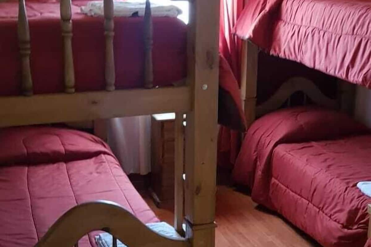 Quarto com duas beliches, cabeceiras de madeira e uma luminária pendente.
