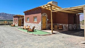 Un bâtiment rustique avec une façade en pierre, une porte en bois et un patio couvert agrémenté de chaises en bois.