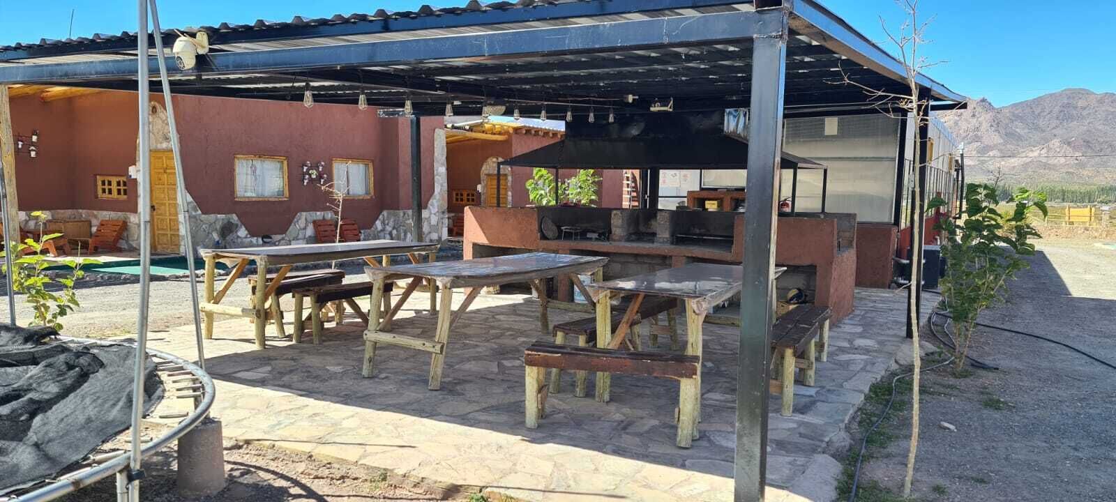 Un patio al aire libre con mesas y bancos de madera rústica, una parrilla y una zona de estar cubierta con vistas a las montañas al fondo.