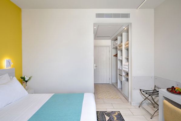 A hotel room with a bed, a bedside table with a lamp, a small plant, and a view into the hallway. - Legacy Nazarethe Hotel (Nazareth)