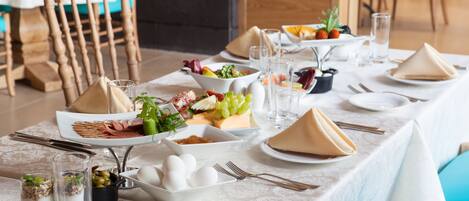 Un desayuno con diversos platos, como huevos, frutas y pan, dispuestos sobre una mesa con mantel blanco.