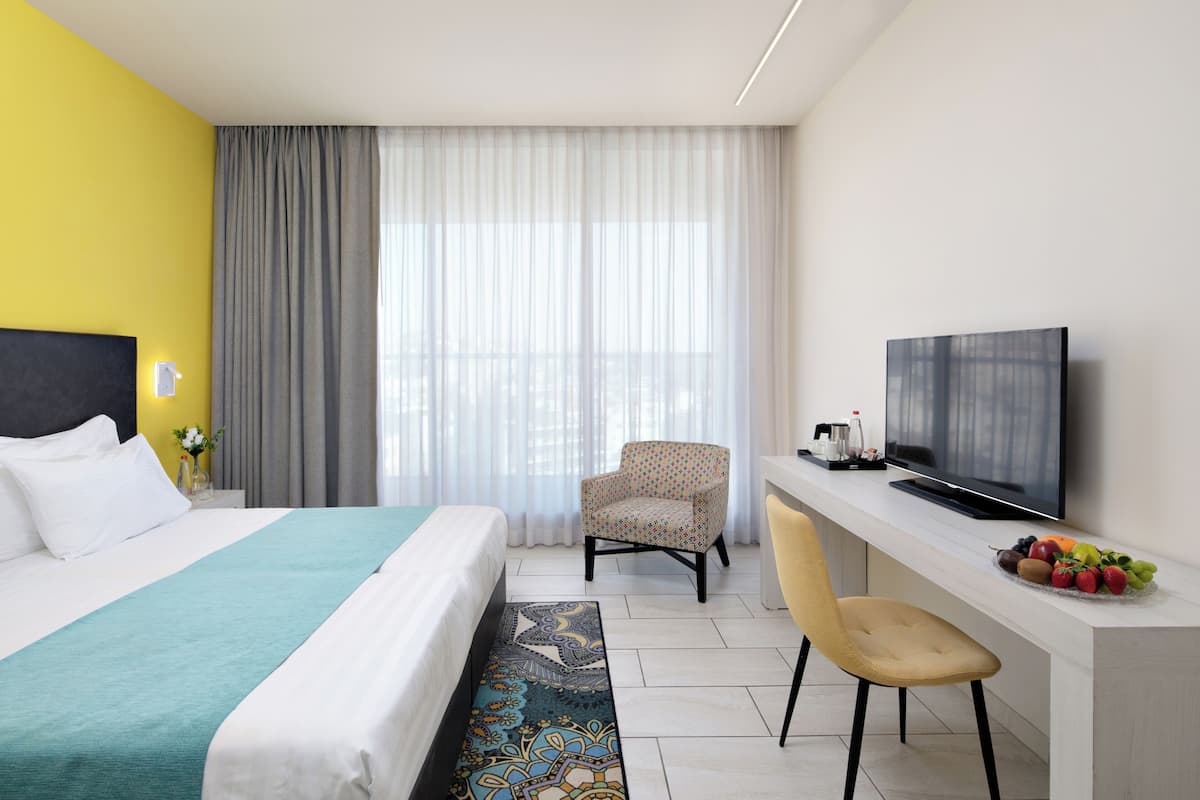 Ein Hotelzimmer mit einem Bett, einem Schreibtisch mit Fernseher, einem Sessel und einer Obstschale.