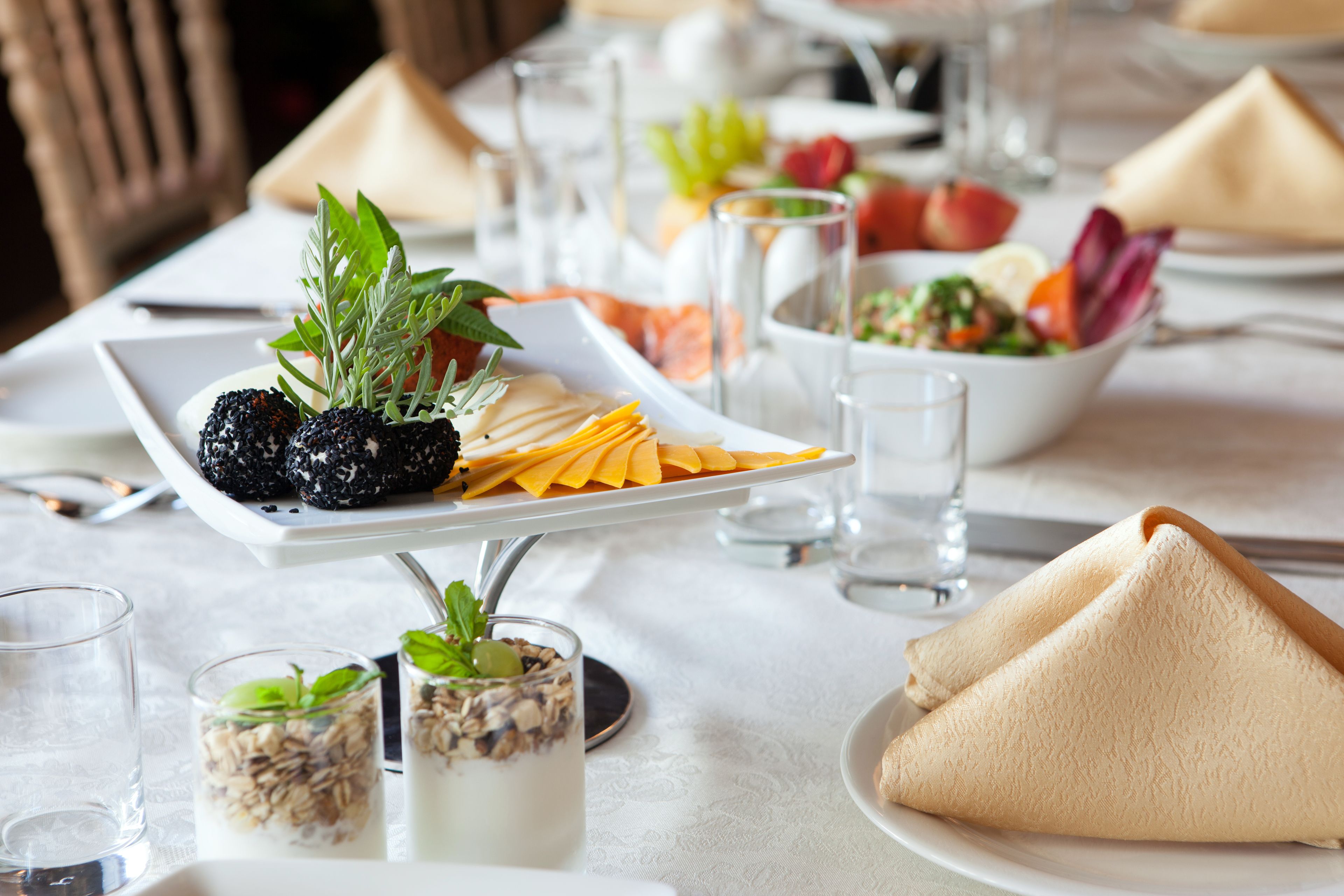 Uma mesa de jantar bem arrumada com diversos alimentos, incluindo uma travessa de amoras, queijo e uma saladeira.