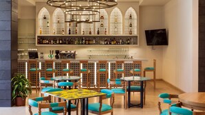 A bar area with multiple shelves of bottles, a television mounted on the wall, and several tables and chairs arranged for seating. - Legacy Nazarethe Hotel (Nazareth)