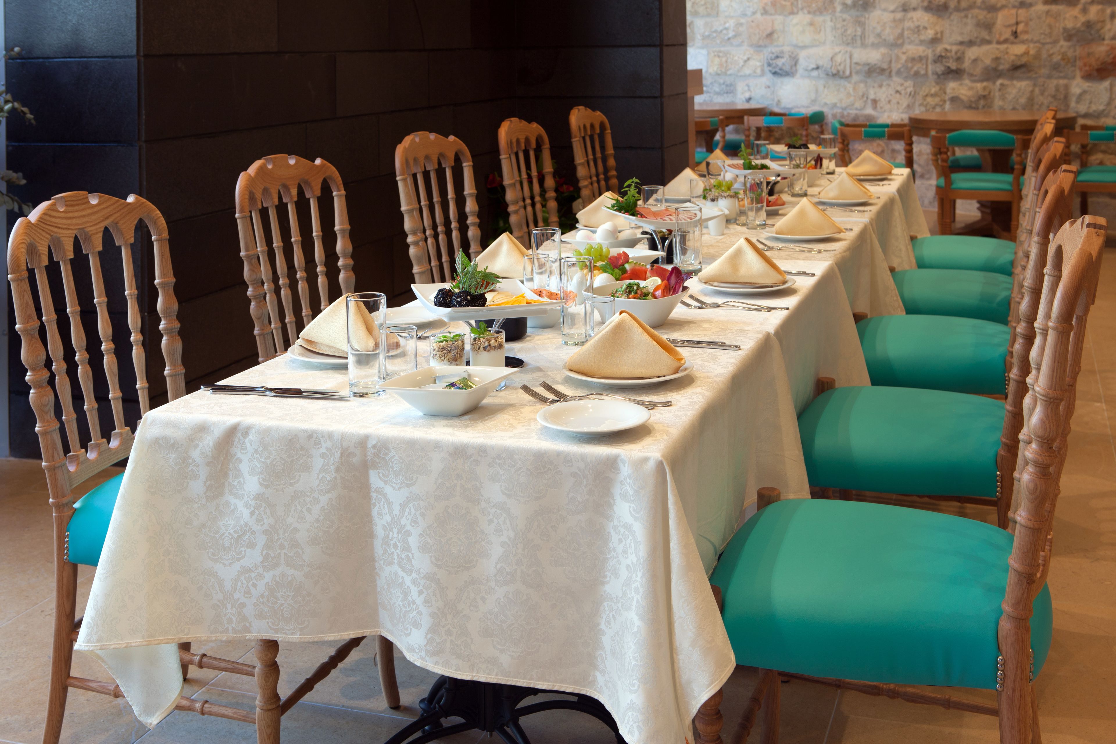 A long dining table set with white tablecloths, teal chairs, and various dishes and glasses.