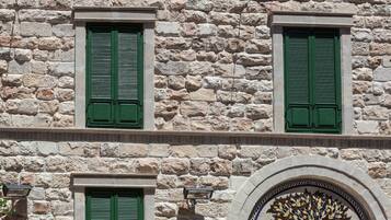 A stone building with green shutters, a tiled patio with outdoor seating, and a decorative mural.