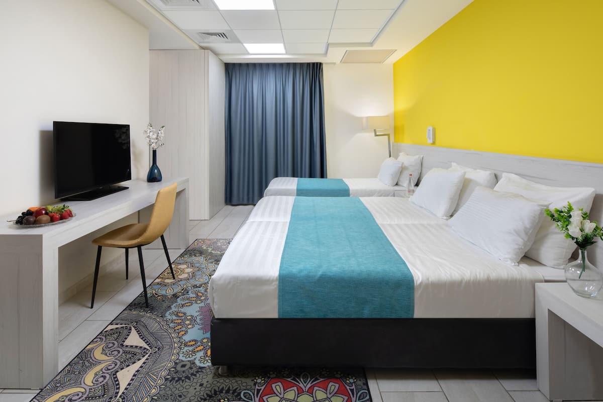 Ein Hotelzimmer mit einem Bett, einem Schreibtisch mit Fernseher, einem Sessel und einem Fenster mit Vorhängen.