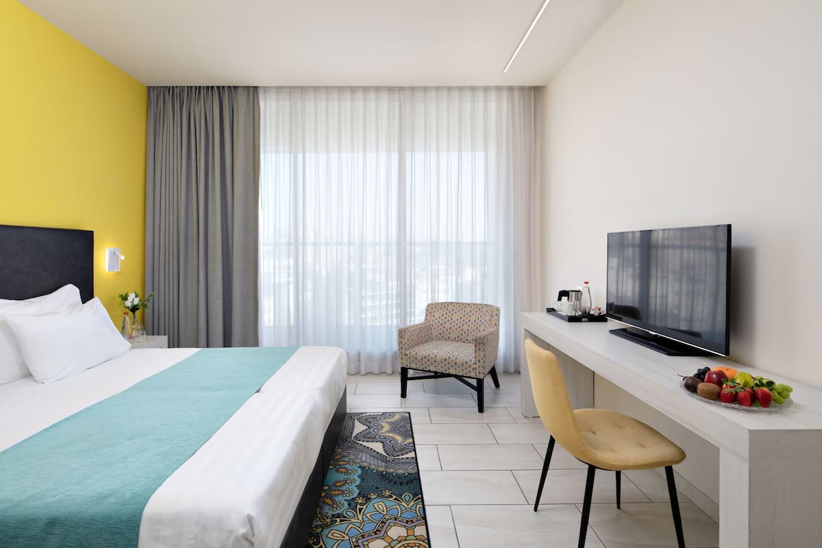 Ein Hotelzimmer mit einem Bett, einem Schreibtisch mit Fernseher, einem Sessel und einer Obstschale.