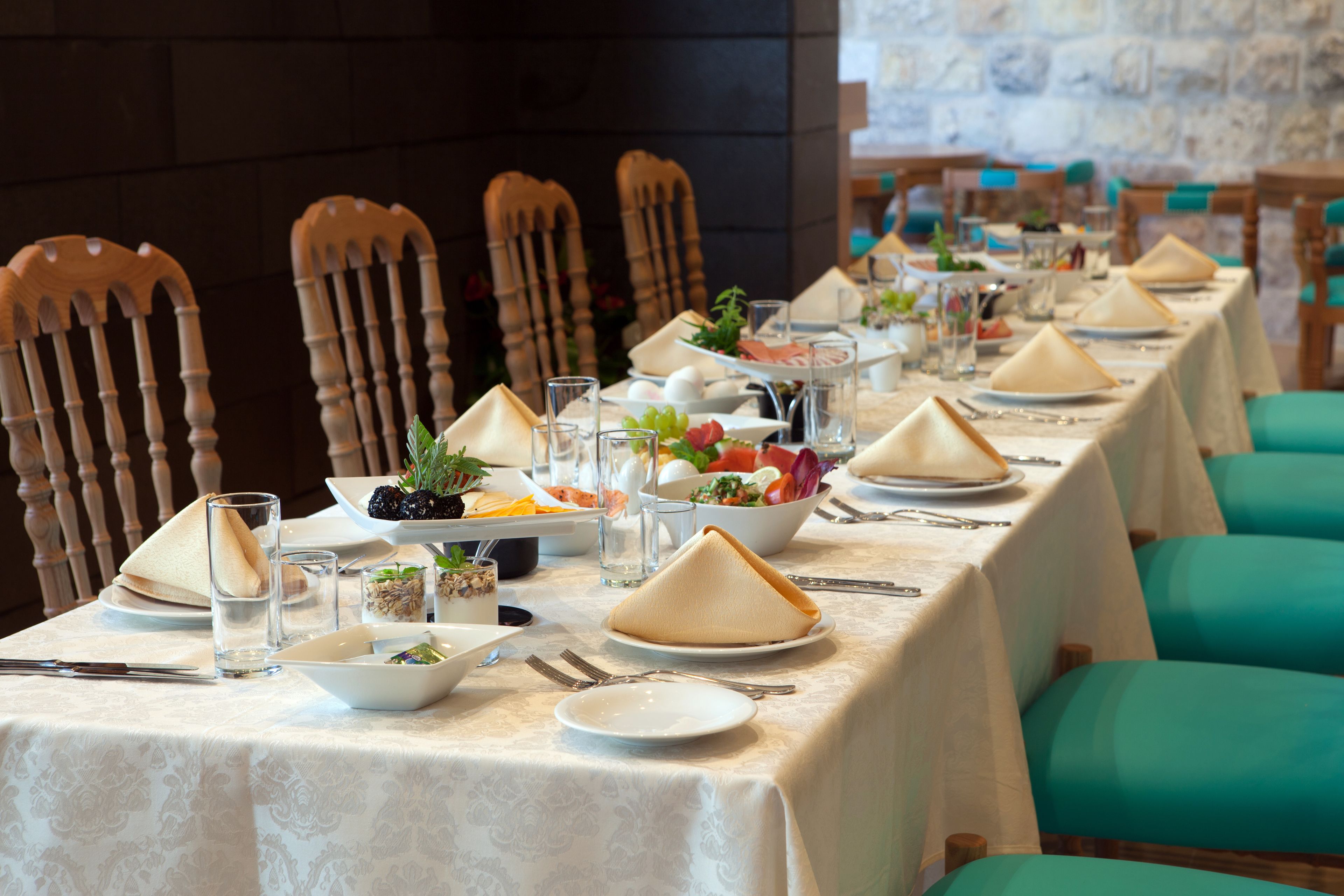 A long dining table set with plates, glasses, and cutlery, surrounded by wooden chairs.