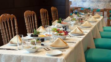 A long dining table set with plates, glasses, and cutlery, surrounded by wooden chairs.