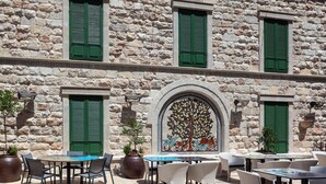 An outdoor seating area with stone walls, green shutters, and a tiled mural. - Legacy Nazarethe Hotel (Nazareth)