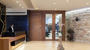 A reception area with a wooden reception desk, a stone wall, and a potted plant. - Legacy Nazarethe Hotel (Nazareth)