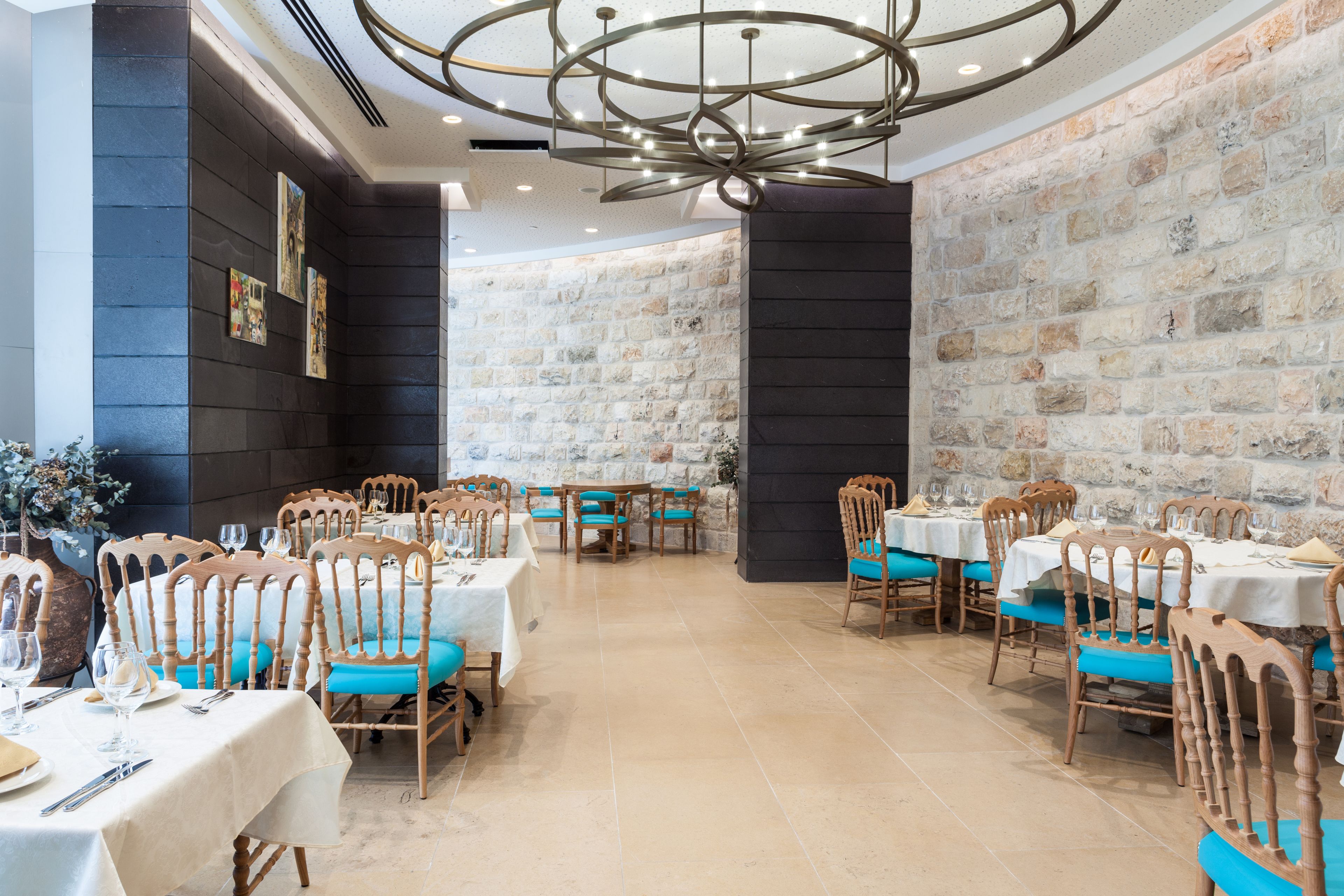 A restaurant with wooden chairs and tables, a stone wall, and a modern chandelier.