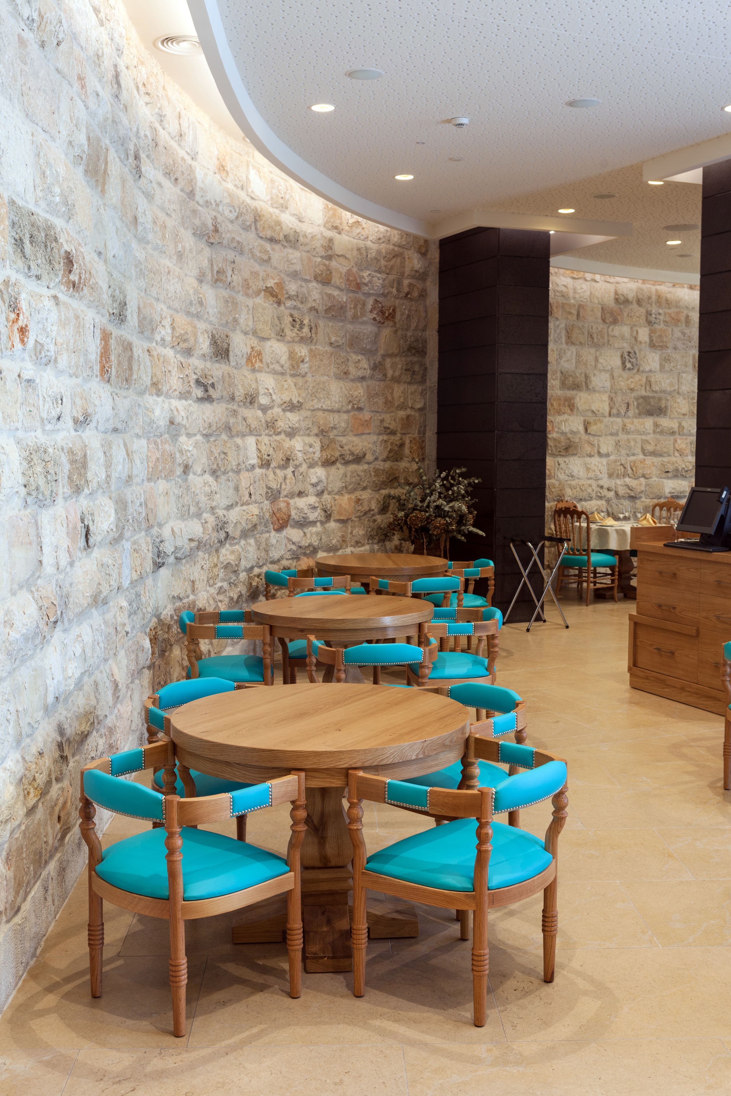 A stone-walled dining area with wooden tables and turquoise chairs.