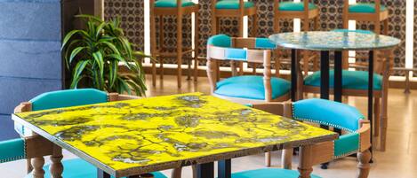 A dining area with wooden chairs and tables, a potted plant, and patterned wallpaper.