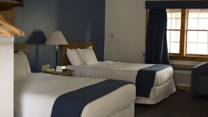 A hotel room with two beds, a nightstand with a lamp, a chair, and a window with curtains. - Rhinebeck Village Inn (Rhinebeck)