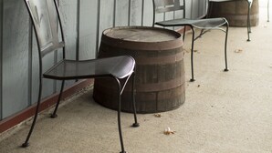 A row of metal chairs and a wooden barrel on a concrete floor against a wooden wall. - Rhinebeck Village Inn (Rhinebeck)