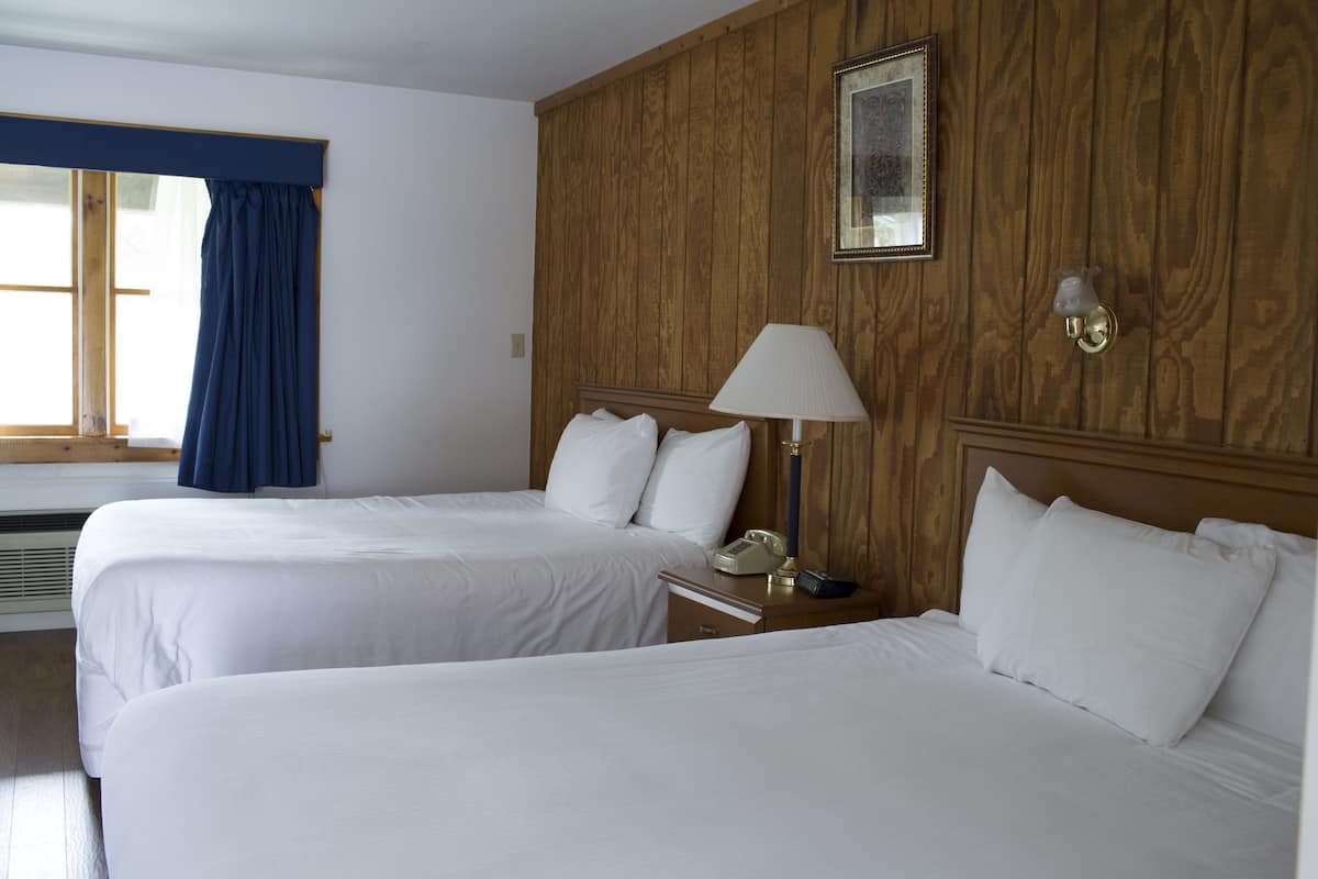 A hotel room with two beds, a nightstand with a lamp, a framed picture on the wall, and a window with blue curtains.