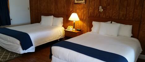 A hotel room with two beds, wooden paneling, a nightstand with a lamp, and a framed picture on the wall.