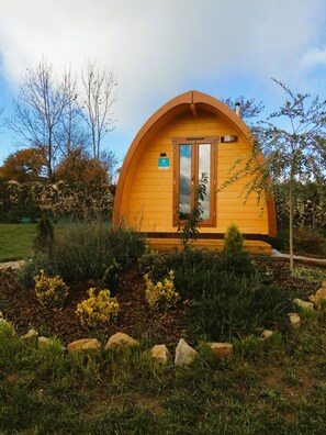 A wooden dome-shaped building with a door and window, surrounded by a landscaped garden with various plants and rocks. - Les Roulottes de la Ferme des Chanaux (Saint-Julien-d'Ance)