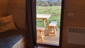 Una cabaña acogedora con interior de madera, una cama, una mesa y sillas afuera, y vistas al exterior.