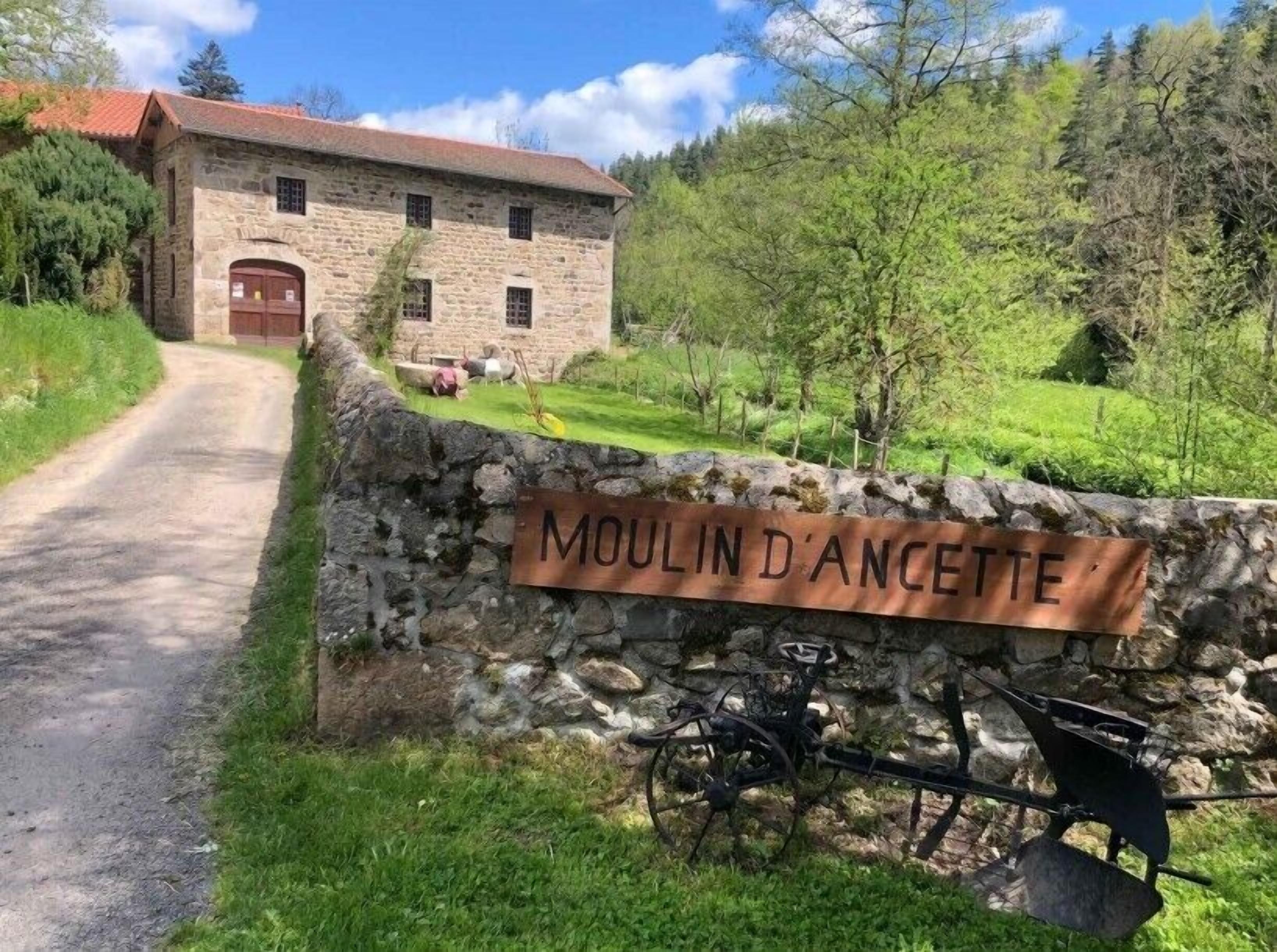 Un edificio de piedra con un letrero que dice "MOULIN D'ANCETTE" y una bicicleta estacionada en la entrada.